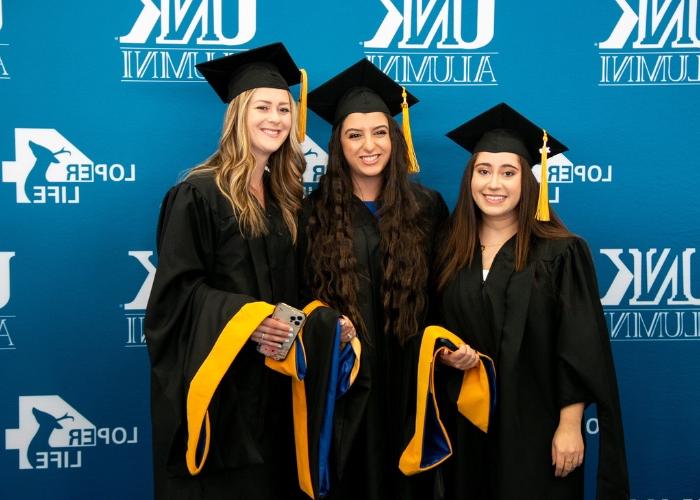 Three graduates posing in front of backdrop.