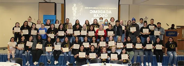 a large group of students pose together holding up certificates